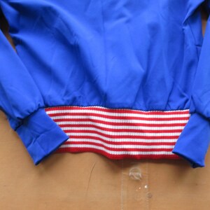 May include: A blue jacket with a red and white striped waistband.