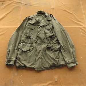 Puede incluir: Una chaqueta verde de estilo militar con cintura de cordón y varios bolsillos.