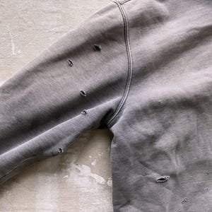 May include: A gray sweatshirt with several small holes throughout the fabric. The sweatshirt has a hood and long sleeves.