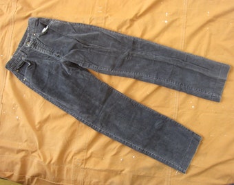 May include: A pair of dark gray corduroy pants laid out on a brown fabric background.