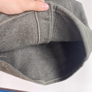 May include: A dark olive green felted wool cap featuring a structured crown and a thick, folded brim. The interior shows a matching dark olive green felt lining with visible stitched seams along the inner band and a reinforced top panel.