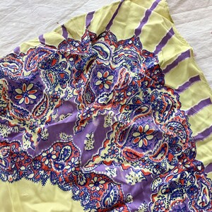 May include: A vintage paisley scarf with a yellow border and a central design in shades of purple, red, and blue. The scarf features a detailed floral and teardrop pattern, creating a vibrant and eye-catching accessory.