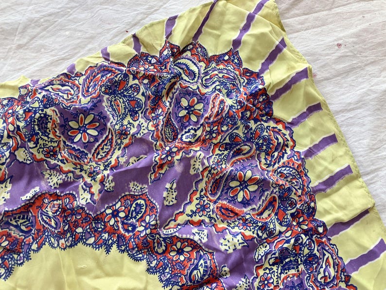 May include: A vintage paisley scarf with a yellow border and a central design in shades of purple, red, and blue. The scarf features a detailed floral and teardrop pattern, creating a vibrant and eye-catching accessory.