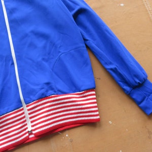 May include: A blue jacket with a white zipper and red and white striped trim.
