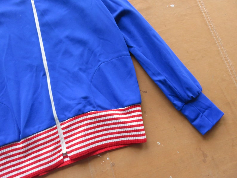 May include: A blue jacket with a white zipper and red and white striped trim.