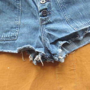 Op de afbeelding: Een blauwe denim short met een rafelige zoom. De short heeft een knoopsluiting en twee zakken aan de voorkant.