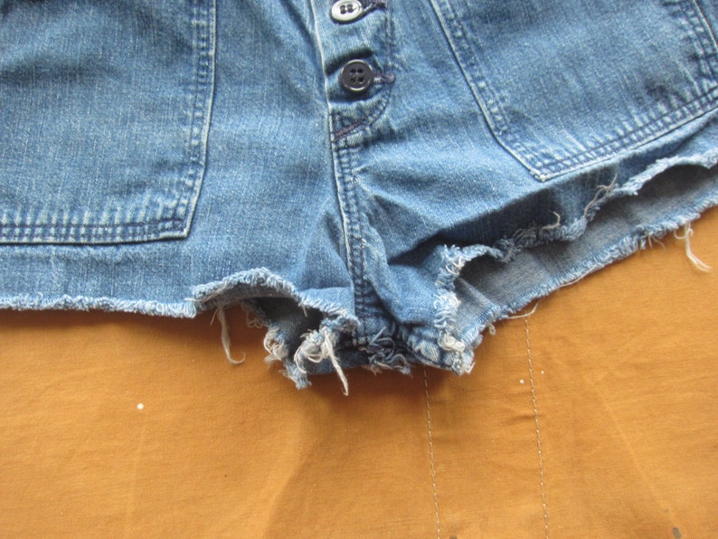 Op de afbeelding: Een blauwe denim short met een rafelige zoom. De short heeft een knoopsluiting en twee zakken aan de voorkant.