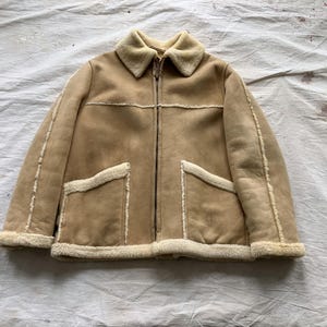 May include: A tan suede jacket with a white shearling collar and lining. The jacket has a zip closure and two front pockets.