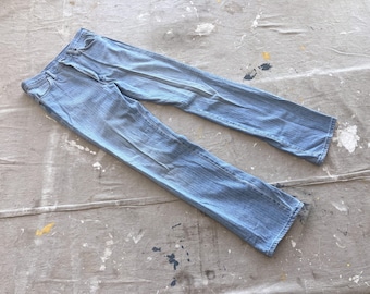 May include: A pair of light blue denim jeans laid flat on a gray surface. The jeans have a classic straight leg style.