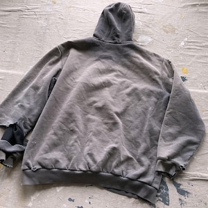 May include: A gray hooded sweatshirt with a distressed look. The sweatshirt has a faded appearance and a loose fit.
