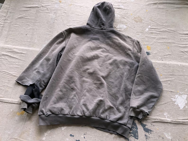 May include: A gray hooded sweatshirt with a distressed look. The sweatshirt has a faded appearance and a loose fit.