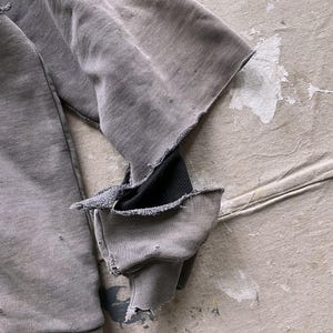 May include: A gray sweatshirt with a distressed look, featuring a black fabric patch on the elbow and frayed edges.