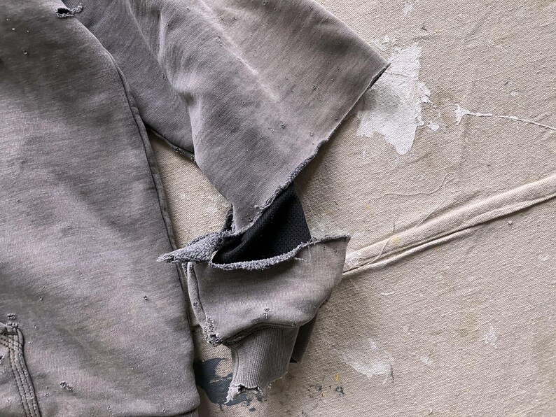 May include: A gray sweatshirt with a distressed look, featuring a black fabric patch on the elbow and frayed edges.