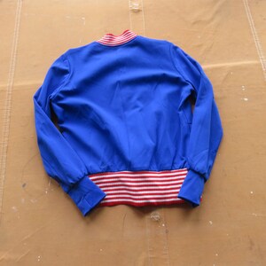 May include: A blue bomber jacket with red and white striped trim around the cuffs and waistband.