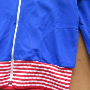 May include: A blue and white striped jacket with a zipper closure. The jacket has a red and white striped band at the bottom.