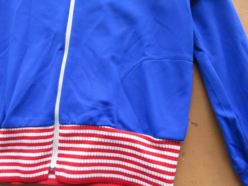 May include: A blue and white striped jacket with a zipper closure. The jacket has a red and white striped band at the bottom.