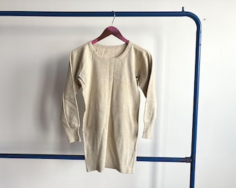May include: A long-sleeved, crew-neck top in a light beige, heathered fabric. The garment features ribbed cuffs at the wrists and a ribbed neckline, hanging from a purple hanger on a blue metal rack against a plain white background.