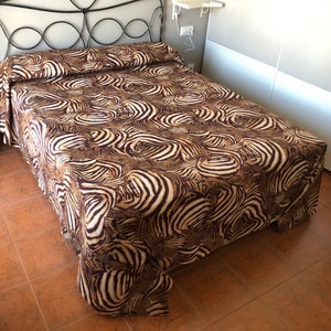 May include: A brown and white zebra print bedspread with a black metal bed frame.