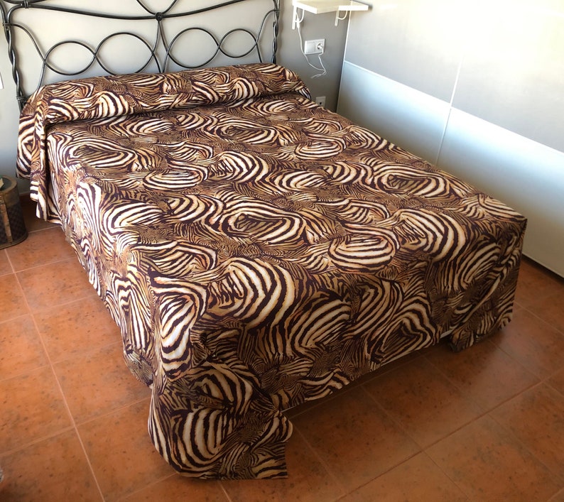 May include: A brown and white zebra print bedspread with a black metal bed frame.