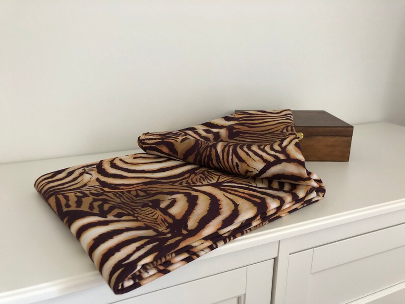 May include: A brown and tan zebra print fabric folded on a white surface. The fabric is folded in half and the edges are visible.