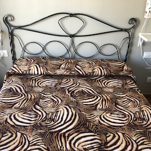 May include: A bed with a black metal headboard and a zebra print duvet cover. The duvet cover is made of a soft, comfortable fabric and features a bold zebra print in shades of brown, black, and white.