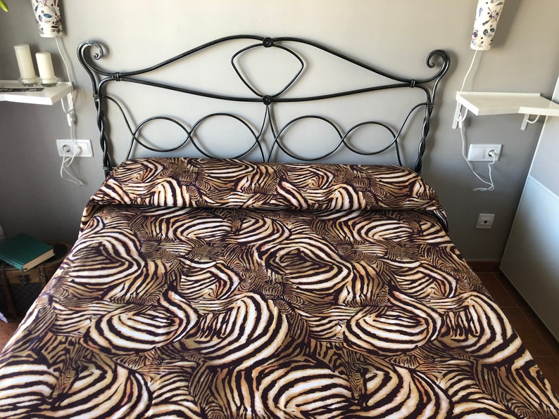 May include: A bed with a black metal headboard and a zebra print duvet cover. The duvet cover is made of a soft, comfortable fabric and features a bold zebra print in shades of brown, black, and white.