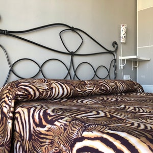May include: A black metal bed frame with a headboard featuring intricate scrollwork. The bed is made up with brown and white zebra print bedding.