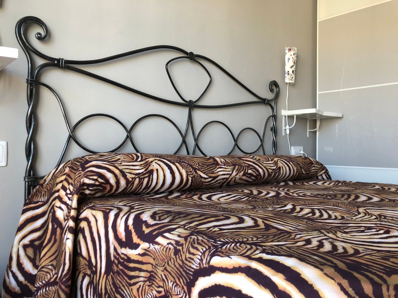May include: A black metal bed frame with a headboard featuring intricate scrollwork. The bed is made up with brown and white zebra print bedding.