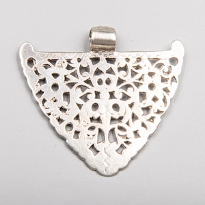 Può includere: Un ciondolo d'argento con una forma triangolare e un intricato design traforato. Il ciondolo ha un anello nella parte superiore per una catena. Il design presenta motivi floreali e geometrici, creando un aspetto delicato e ornato. Il ciondolo è probabilmente in argento sterling.