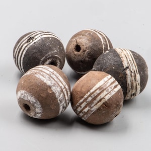 May include: Five round, stone-like beads in varying shades of brown and dark gray. Each bead features white, diagonal stripes. The beads have a hole drilled through the center, suggesting they are for stringing.