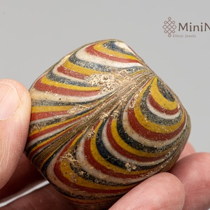 May include: A close-up of a colourful glass bead with a swirling pattern of red, yellow, white, and blue. The bead is being held in a hand.