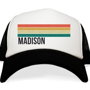 May include: A white and black trucker hat with a vintage-style rainbow stripe design and the word "MADISON" in black text.
