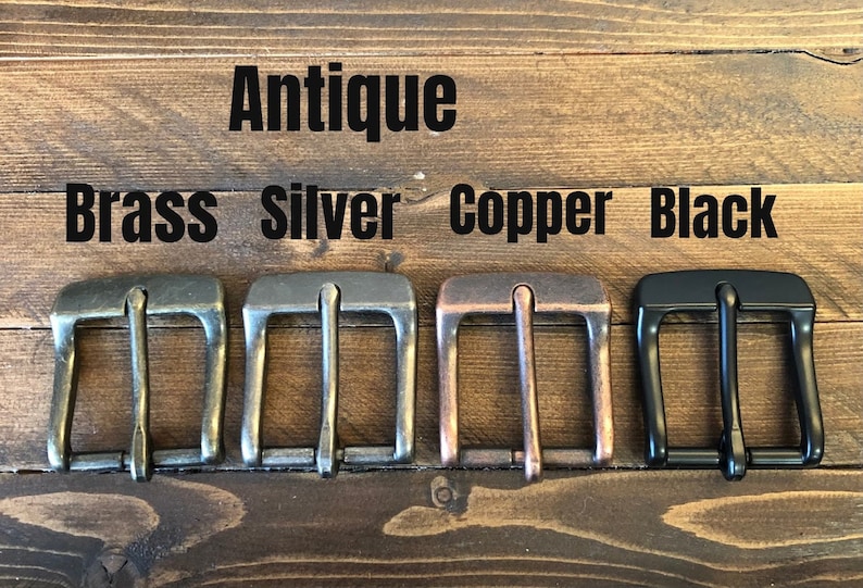 May include: Five metal belt buckles in different finishes: antique brass, silver, copper, and black. The buckles are arranged in a row from left to right.