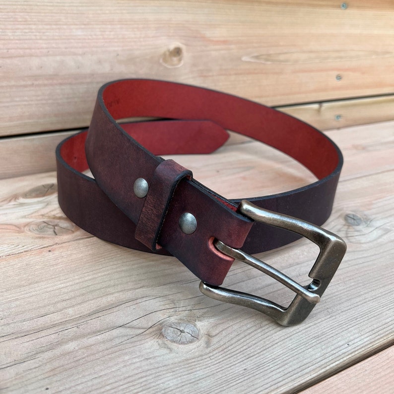 May include: A dark brown leather belt with a red lining and a silver buckle.