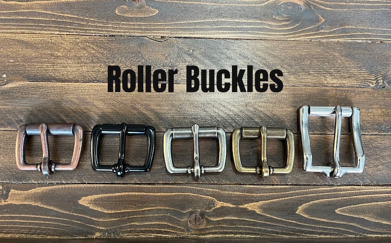 May include: Five metal roller buckles arranged in a row, featuring copper, black, brushed silver, antique brass, and polished silver finishes. The text Roller Buckles is printed in black above the hardware, which includes a frame, prong, and roller.