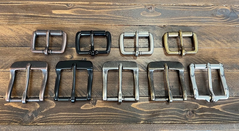 May include: A set of ten metal belt buckles in various finishes, including antique brass, silver, black, and nickel. The buckles are all the same size and shape, with a rectangular frame and a double prong closure.
