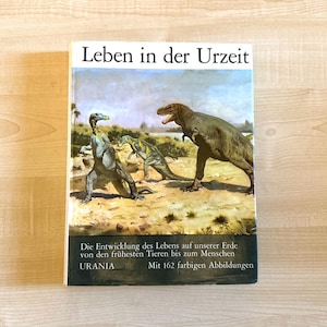Könnte beinhalten: Ein gebundenes Buch mit dem Titel Leben in der Urzeit, das eine prähistorische Landschaft mit drei Dinosauriern zeigt. Der Einband enthält den Text Die Entwicklung des Lebens auf unserer Erde von den frühesten Tieren bis zum Menschen und URANIA.