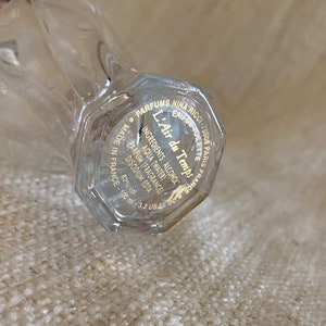 May include: A clear glass bottle with a gold label that reads "Parfums Nina Ricci - 75008 Paris France - Eau de Toilette - L'Air du Temps - Ingredients: Alcohol, Aqua (Water), Parfum (Fragrance), Disodium EDTA - 82% vol. - 100 ml - 3.3 US fl oz - Made in France"