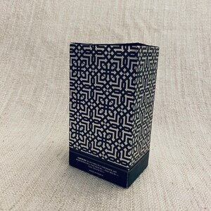 Puede incluir: Una caja con un patr&oacute;n en blanco y negro con el texto "CONTAINS: 50 ALCOHOL, W.C. FRAGRANCE, BHT, BENZYL SALICYLATE, PARFUM, CI 15985, CI 19140, CI 14700, YELLOW NO. 5, CI 15850, RED NO. 4, MADE IN FRANCE".