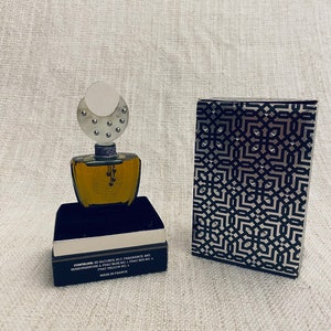 Puede incluir: Un frasco de perfume negro y plateado con una tapa plateada y un patr&oacute;n geom&eacute;trico en la caja. El frasco contiene un l&iacute;quido transparente y la caja tiene el texto "CONTAINS 50 ALCOHOL 35-C. FRAGRANCE MIT RENZOFUENONE - FD&C BLUE NO. 1 FD&C RED NO. 4 FD&C YELLOW NO. 1 MADE IN FRANCE".