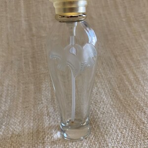May include: A clear glass bottle with a silver top and a white floral design. The bottle is empty and has a small opening at the top.