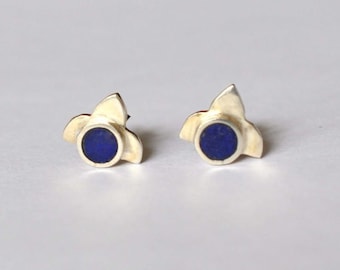 May include: A pair of silver earrings with a blue stone in the center of each earring. The earrings are shaped like a flower with three petals.