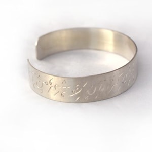 May include: A silver bangle bracelet with an engraved Arabic inscription.