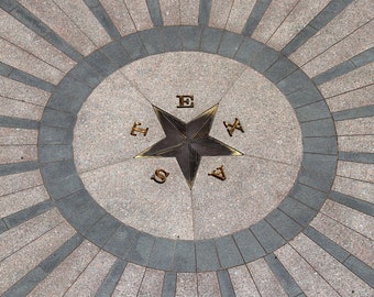 May include: A gray and black star with the word "TEXAS" spelled out around it in gold letters. The star is set in a circular pattern of gray and black tiles.