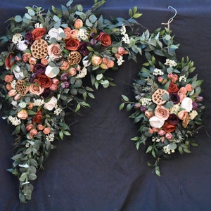 May include: Two cascading floral arrangements in shades of burgundy, peach, and cream, with greenery and dried elements, resembling a world map.