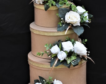 Könnte beinhalten: Vier braune Pappkartons mit goldenen Verzierungen, die übereinander gestapelt sind. Jede Schachtel ist mit einem Strauß weißer Rosen und grünen Blättern verziert.
