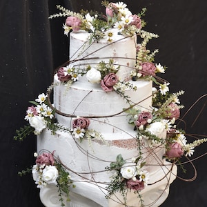 May include: A white wedding cake with three tiers decorated with pink and white flowers and vines.