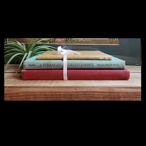 May include: A stack of three vintage hardcover books with a white ribbon tied around them. The top book is green and says "GREEN KNOWE" on the spine. The middle book is yellow and the bottom book is red.