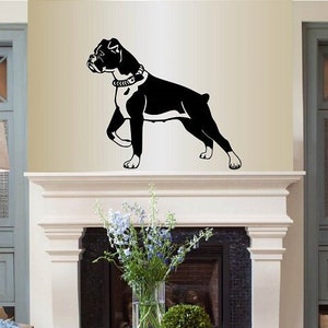 Op de afbeelding: Zwart-witte silhouet van een boxer die op een witte schoorsteenmantel boven een open haard staat. De hond kijkt naar de linkerkant van de afbeelding. De open haard heeft een zwarte haard en een witte omlijsting.