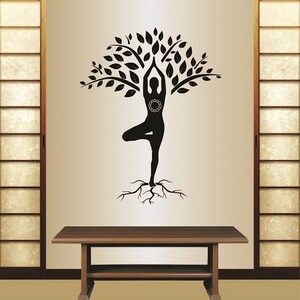 May include: Black and white silhouette of a person in a yoga pose, with roots growing from their feet and forming a tree with leaves. The image is on a beige wall.